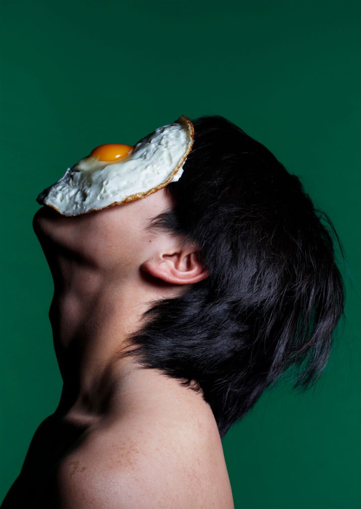 Arabella Guyer - Side profile of a person looking up with a fried egg on their face, with a green background