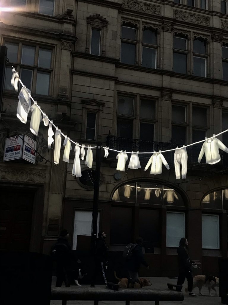 Grace Gibbons - White clothing lit from the inside hangs on a washing line along a darkened street