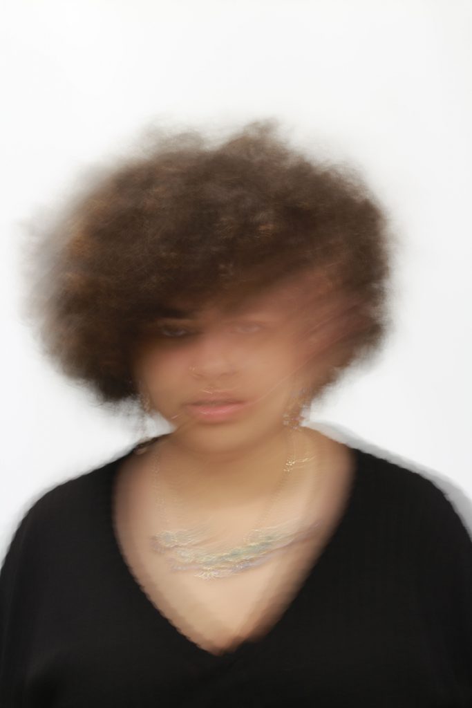 Rhiannon Lancey - Blurred portrait of a person wearing a black top on a white background