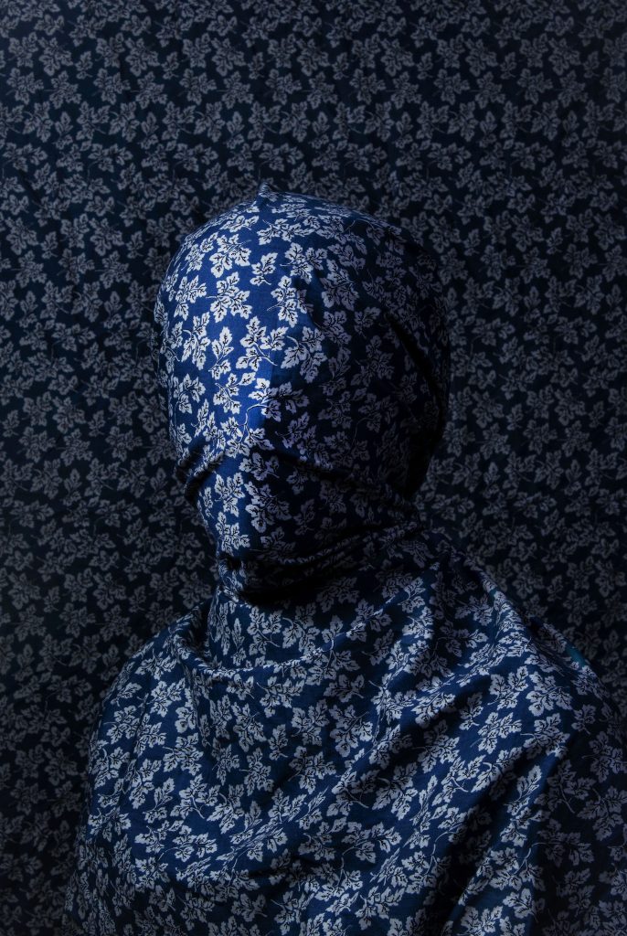 Anzelika Jermosina - Figure covered in draped blue flowery fabric that surrounds them and fills the whole image.