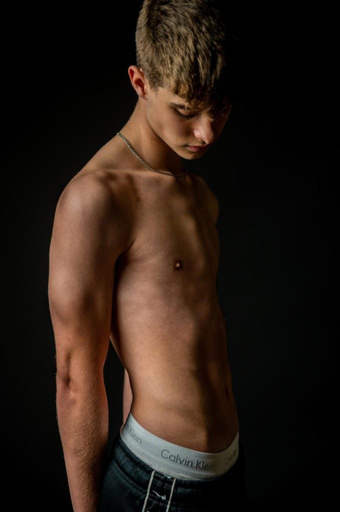 Arabella Rice - Bare-skinned young man partially lit against a black backdrop.