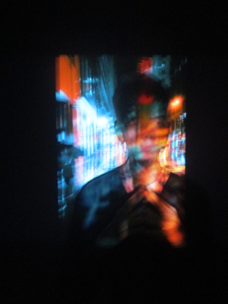 Caleb Yau - Blurred image of a figure surrounded by split blue and red light against a black outline.