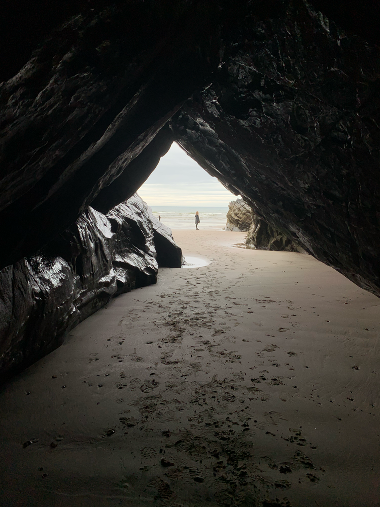 Caleb Yau - A figure standing on a beach is viewed from inside the mouth of a cave.