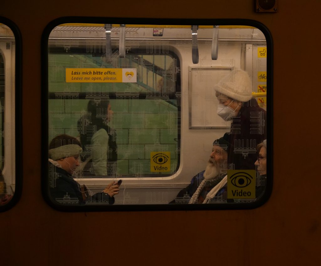 Emily Rahner - View through a train window of passengers sat looking bored.
