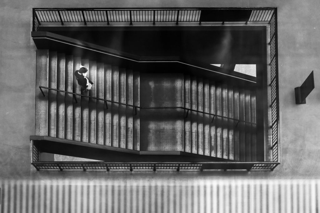 Polly Simpson - Black and white image of a person walking down a double flight of concrete stairs.