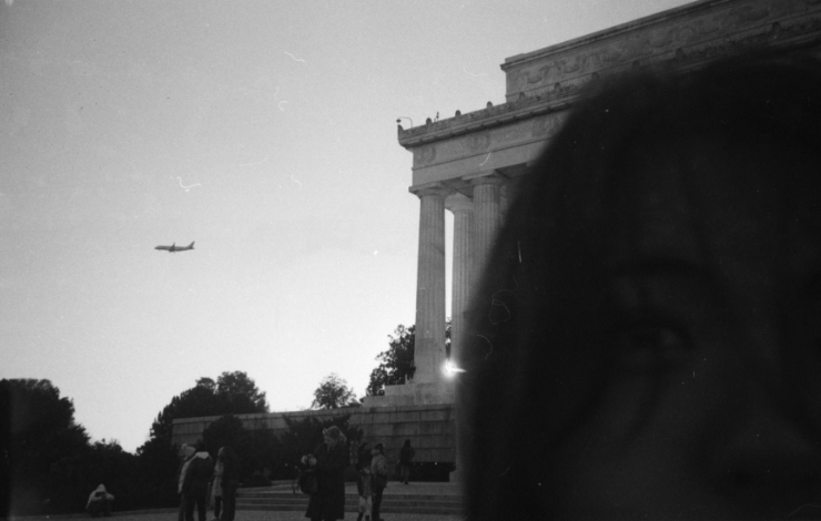 Toby Bayliss - Black and white image of a plane flying next to a grand building with roman columns.